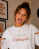 Person wearing a white t-shirt with 'A Little Bit Unhinged' text, pointing at the shirt.