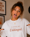 Person wearing a white t-shirt with 'A Little Bit Unhinged' text, pointing at the shirt.